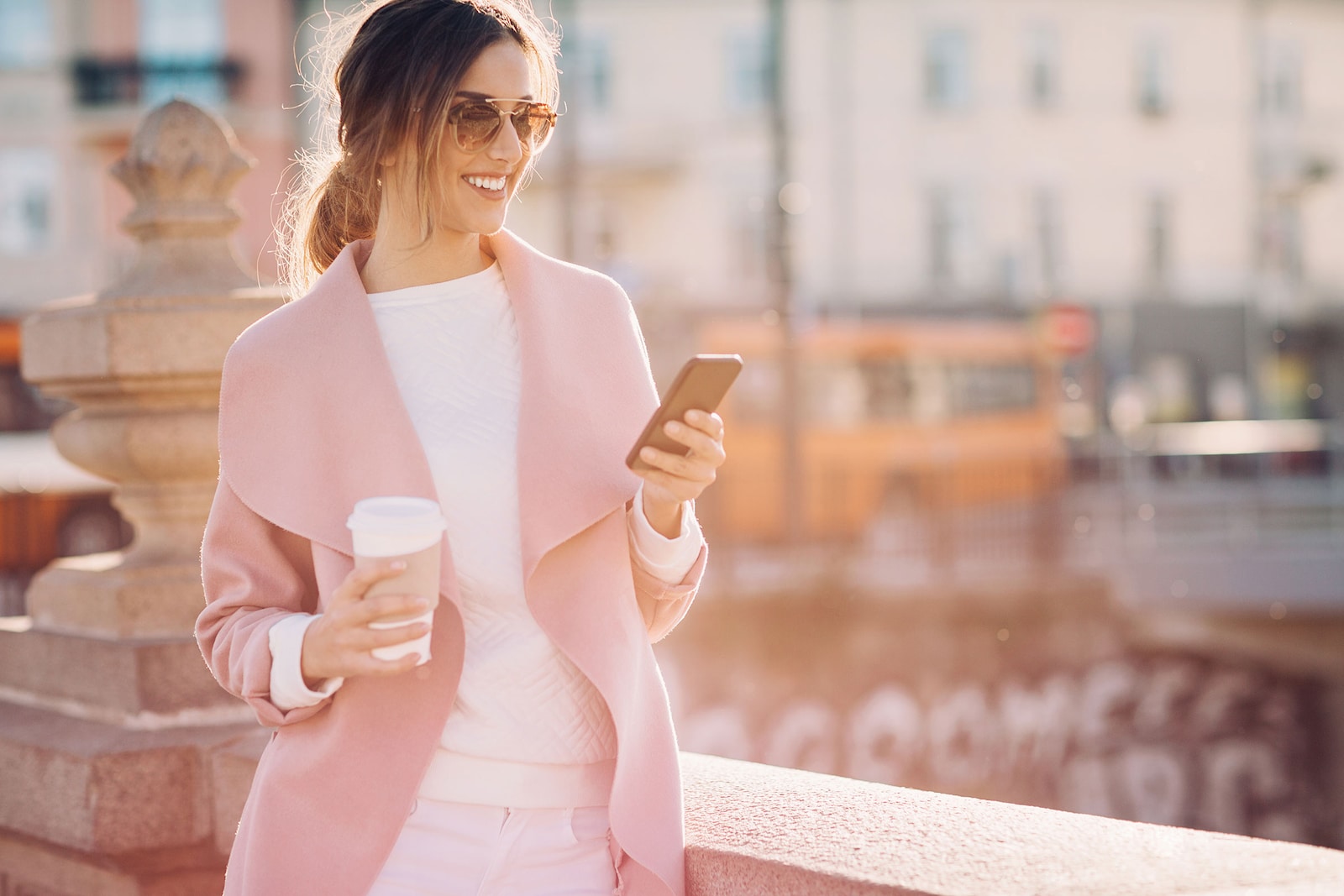 mujer en la calle toma un café mientras chequea su celular